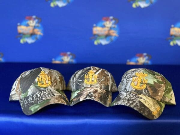 Three camo hats sitting on a blue couch.