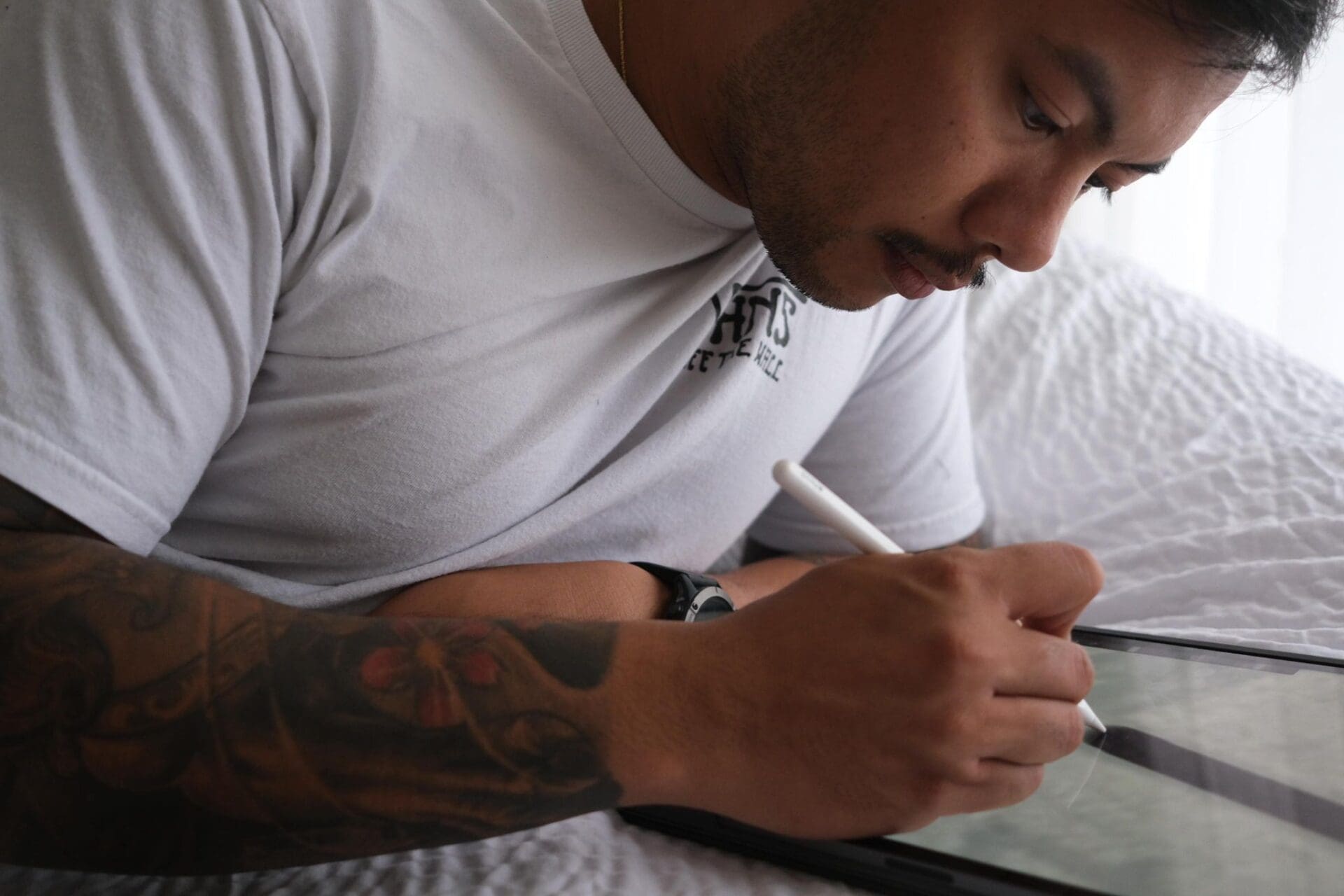 Man with tattoo using stylus on tablet.